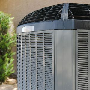 Close-up of an outdoor heat pump condenser unit next to a home wall, showing the metal grille and fan housing used for heating and cooling efficiency.