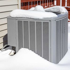 Outdoor heat pump unit covered in snow during winter next to a home exterior