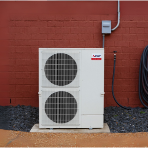 Mitsubishi Electric outdoor mini split heat pump installed against a red brick wall with coiled refrigerant lines and electrical disconnect.