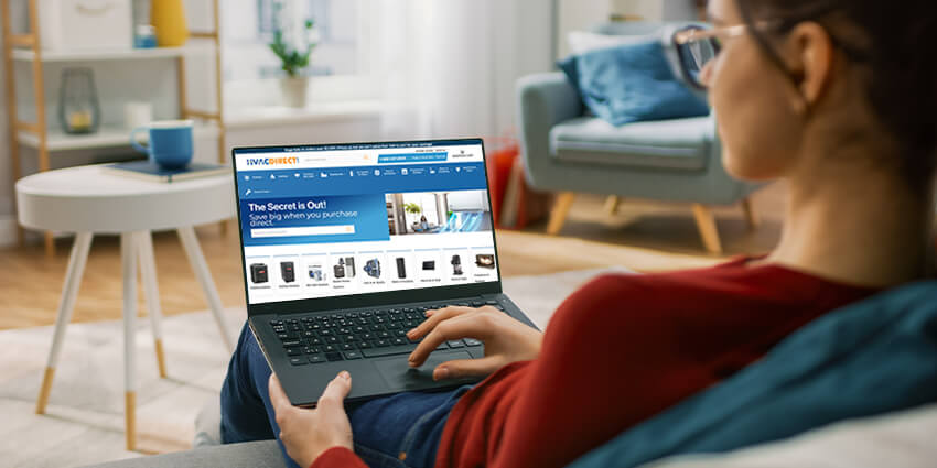 Woman shopping for HVAC systems online at HVACDirect.com using a laptop in a modern living room