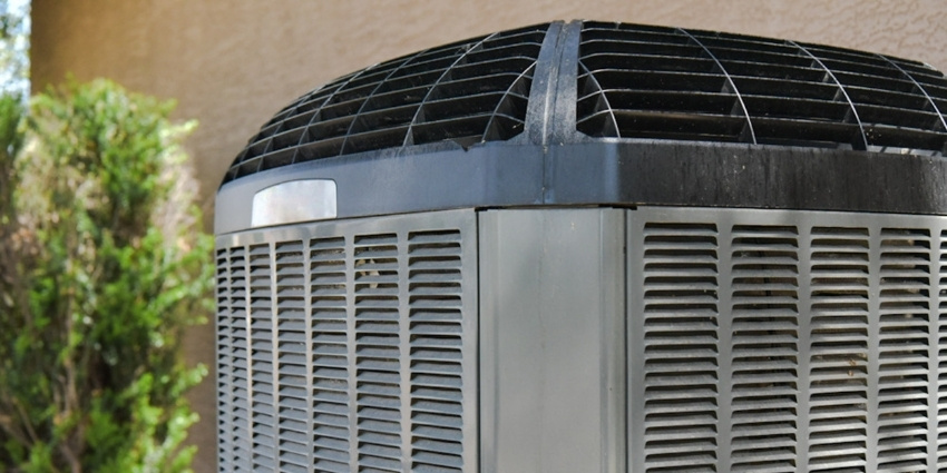 Close-up of an outdoor heat pump condenser unit next to a home wall, showing the metal grille and fan housing used for heating and cooling efficiency.