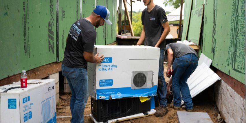 HVAC technicians installing an ACiQ Standard mini split outdoor condenser unit during new home construction