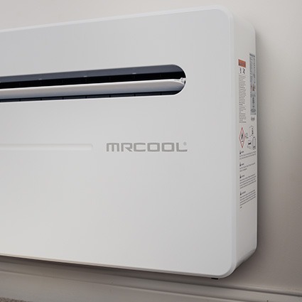 Close-up of a white MRCOOL monoblock wall-mounted air conditioner installed indoors near a baseboard.