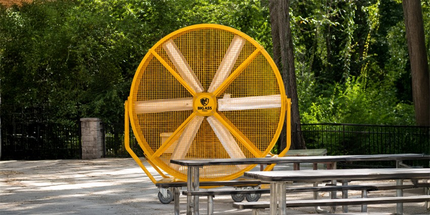 Large yellow portable HVLS fan positioned outdoors near picnic tables, designed to provide high-volume airflow and cooling for open-air environments and event spaces.