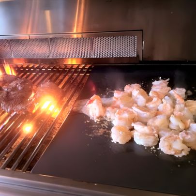 Seafood cooking on built-in gas grill griddle surface with open flame burner