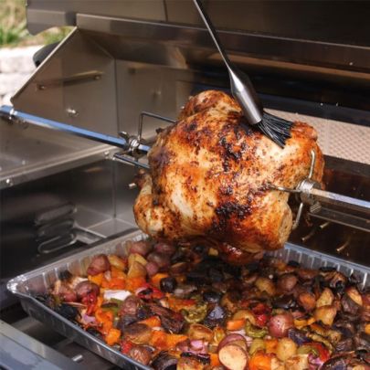 Rotisserie chicken cooking inside built-in gas grill with vegetables below