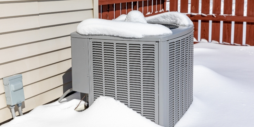 Keep Your Home Warm This Winter with an Efficient Heat Pump Outdoor heat pump unit covered in snow during winter next to a home exterior