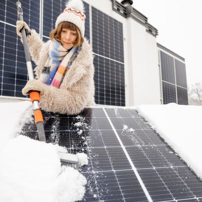 Person brushing snow off solar panels in winter to improve solar energy performance